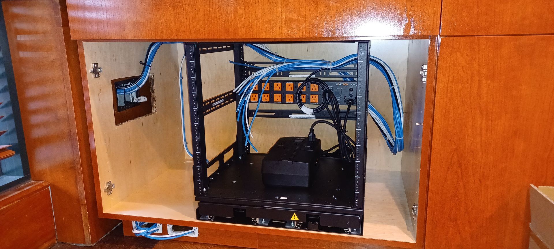 Open cabinet revealing a network rack with blue cables and power outlets.